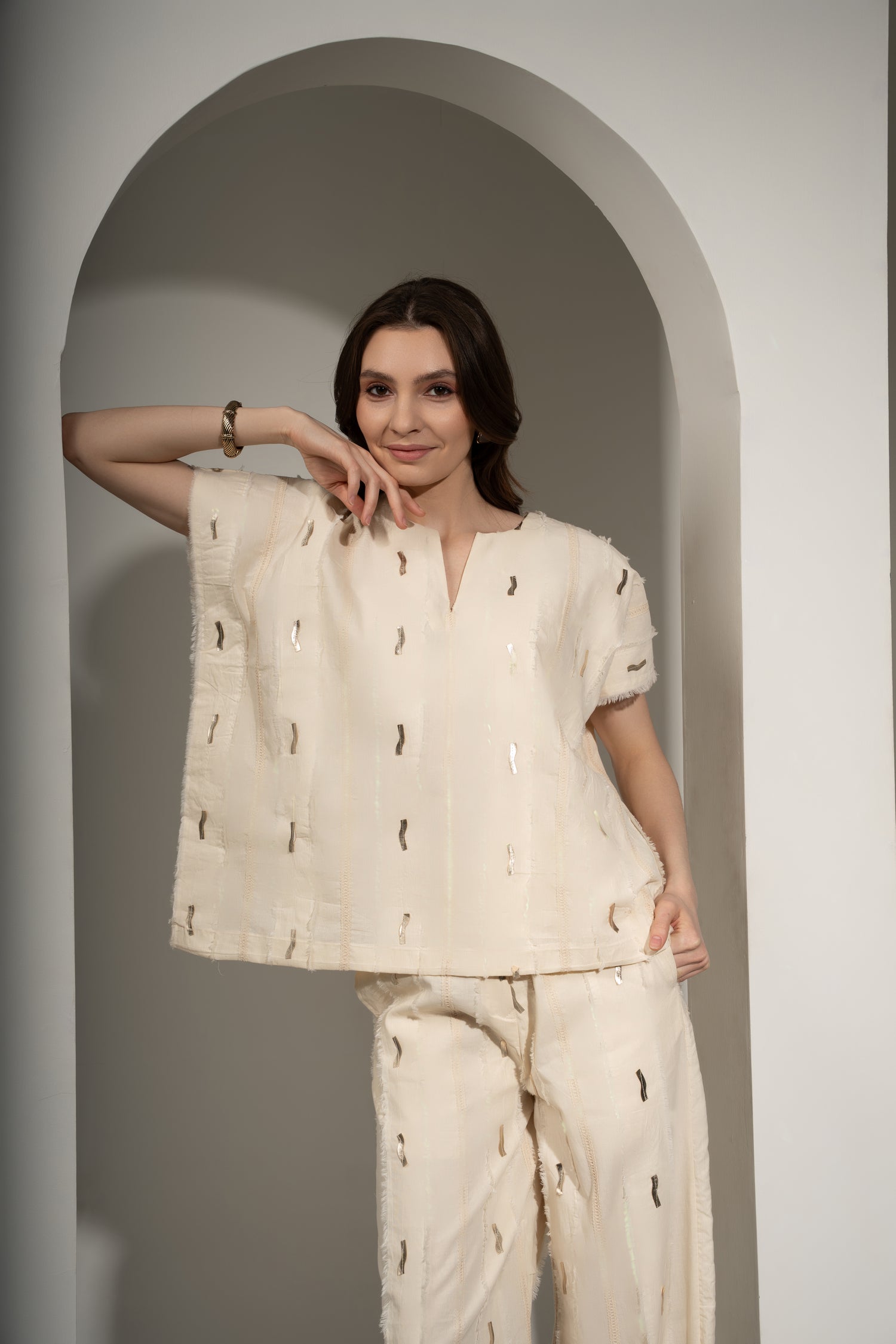 Woman wearing a cream-colored outfit with a textured pattern, standing against a plain background.