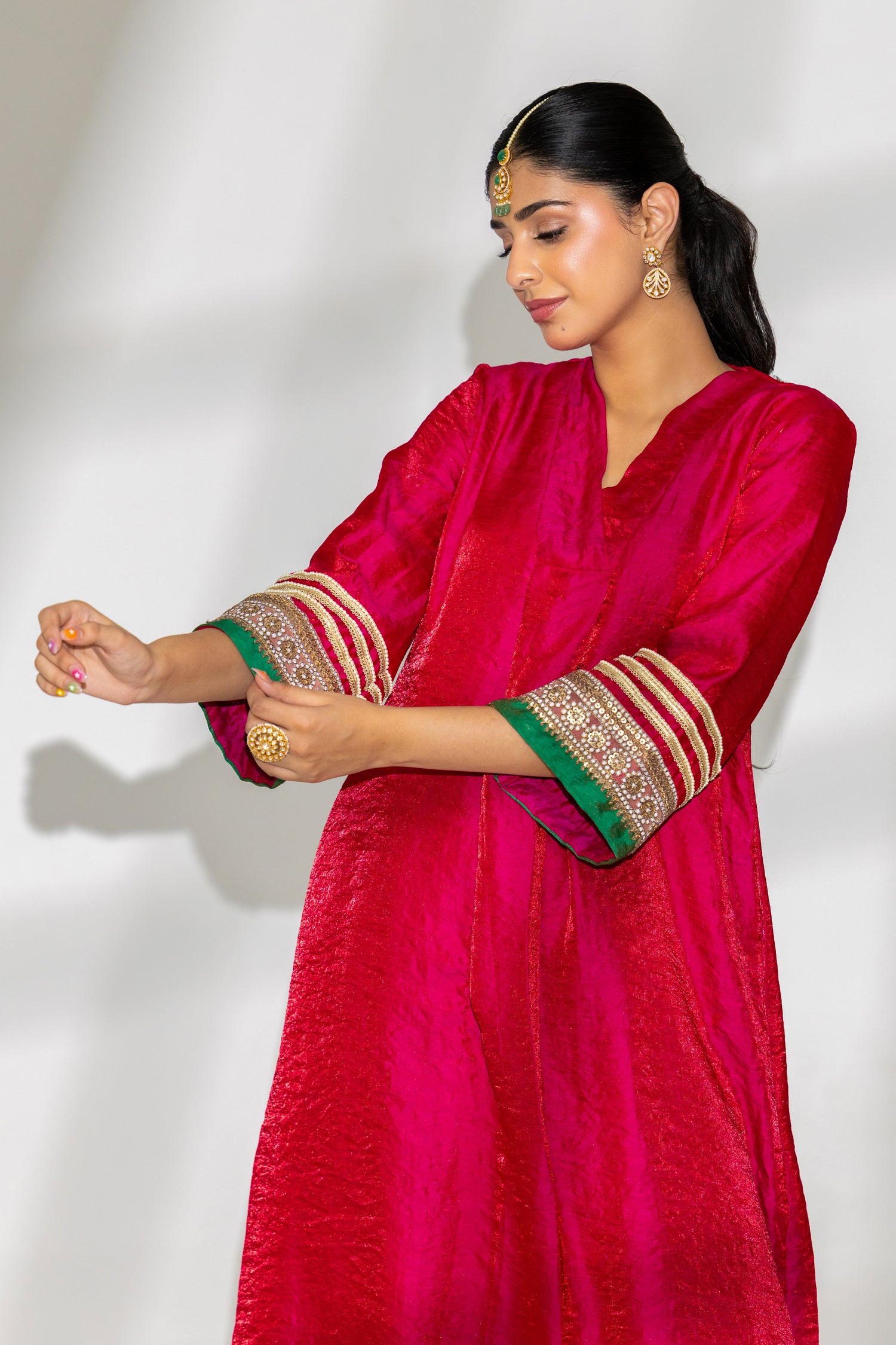 Woman wearing a bright pink traditional outfit with green and gold details on a white background