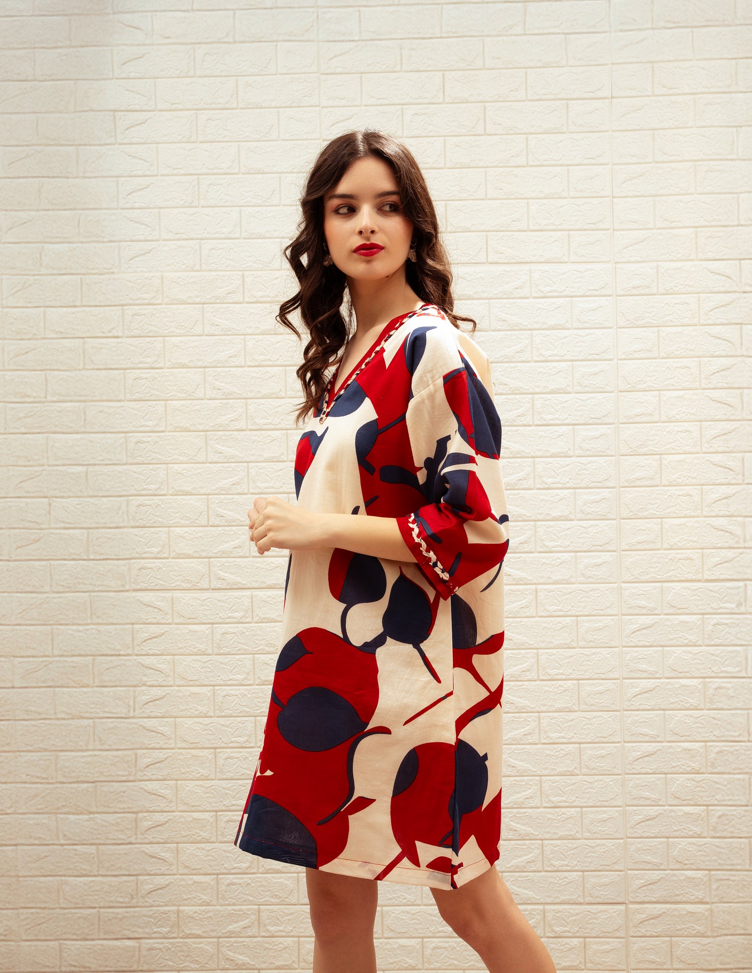 Woman wearing a red and blue patterned dress against a light brick wall.
